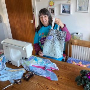 Volunteer wearing a turquiose Incredible Surplus t-shirt, sat at her sewing machine showing us a morsbag she has made.